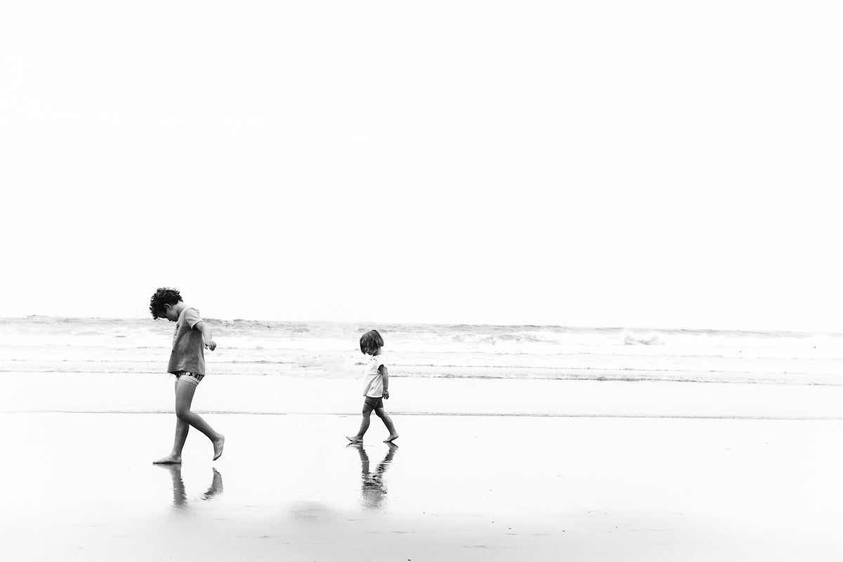Photographie en noir et blanc. Deux enfants sur la plage, silouettes en mouvements, avec la mer et la lumière. A Biarritz. Emma daum photo.